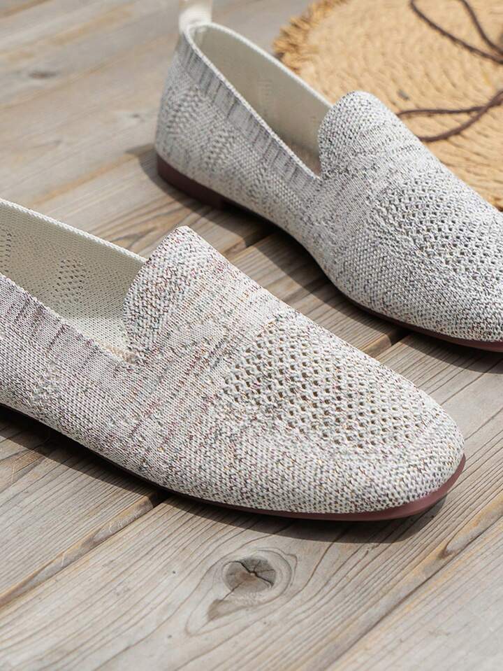 Nærbillede af lysegrå strikkede slip-on sko med hulmønster og rund tå på trægulv. 16