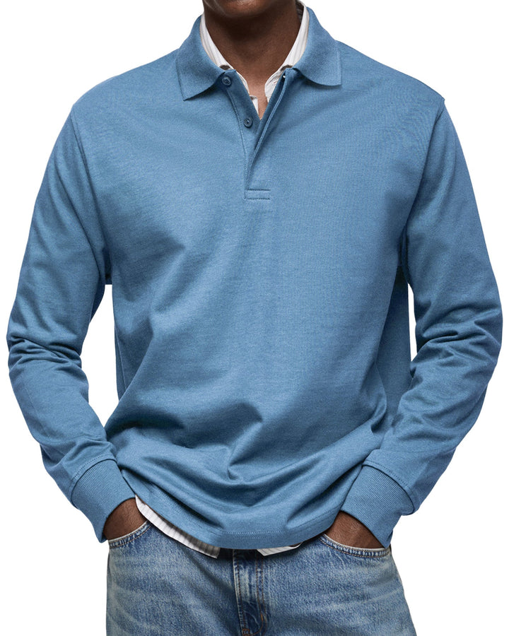 Langærmet poloshirt i lys blå, båret af en model med stribet skjorte under og jeans, set forfra. 2