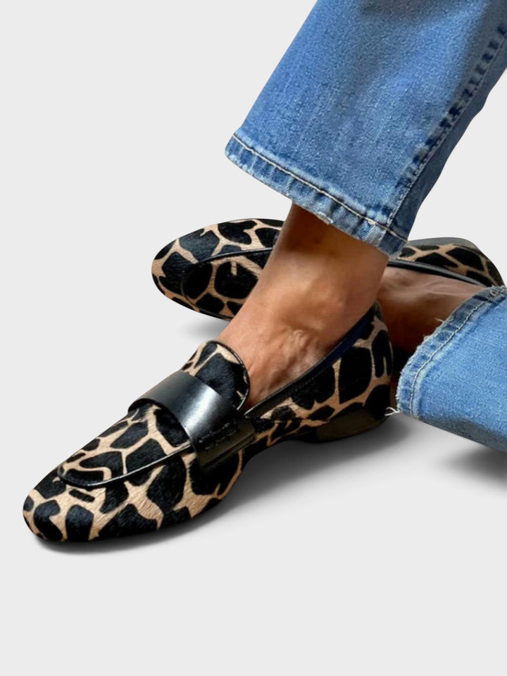 Loafer med sort og beige dyremønster båret til jeans, set skråt fra siden med de to fødder krydset over hinanden. 1