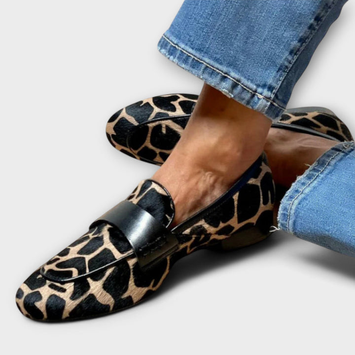 Tætbeskåret billede af loaferen med sort læderbånd over snuden, båret til udslidte jeans, set fra siden mod tåen. 2