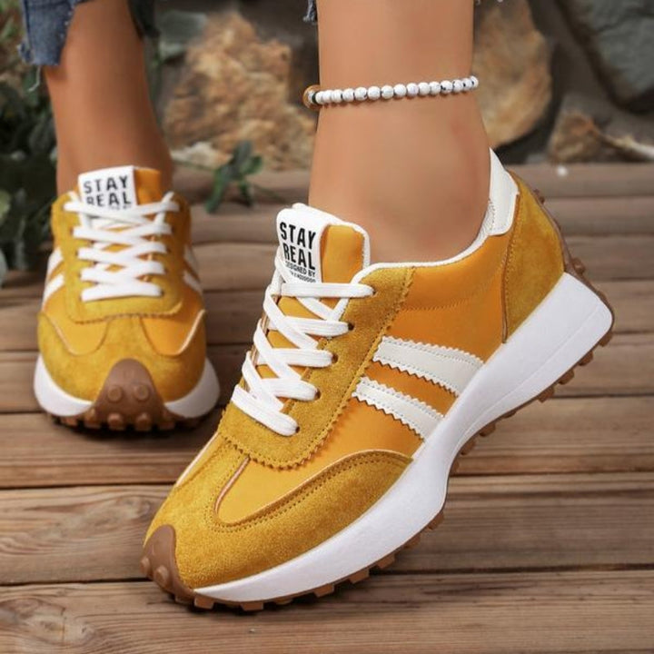 Gule sneakers med hvide striber og tyk plateausål båret af en model på trægulv 6
