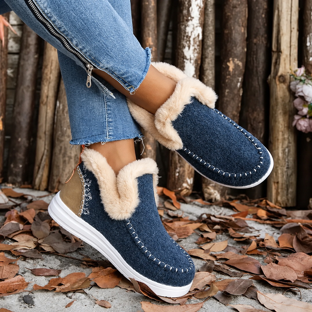 Mørkeblå sneakers med plysfor og lysebrun hælkappe, båret af model med korslagte ben og lynlås på jeans. 4