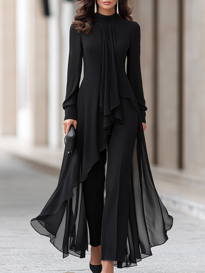 Model i sort chiffon-tunika med høj hals og draperet tørklæde, kombineret med bukser med vide ben, set fra taljen og ned på en gade. 1