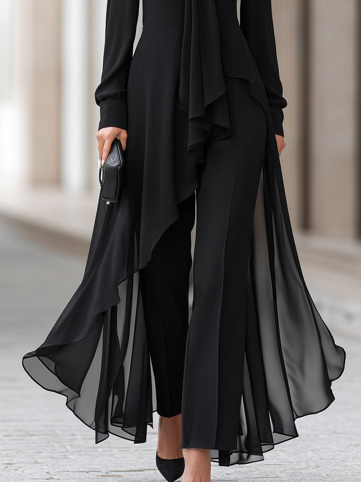 Detalje af de vide bukser og den asymmetriske, gennemsigtige chiffon-tunika, der flyder ned over benene, med sorte spidse sko. 4