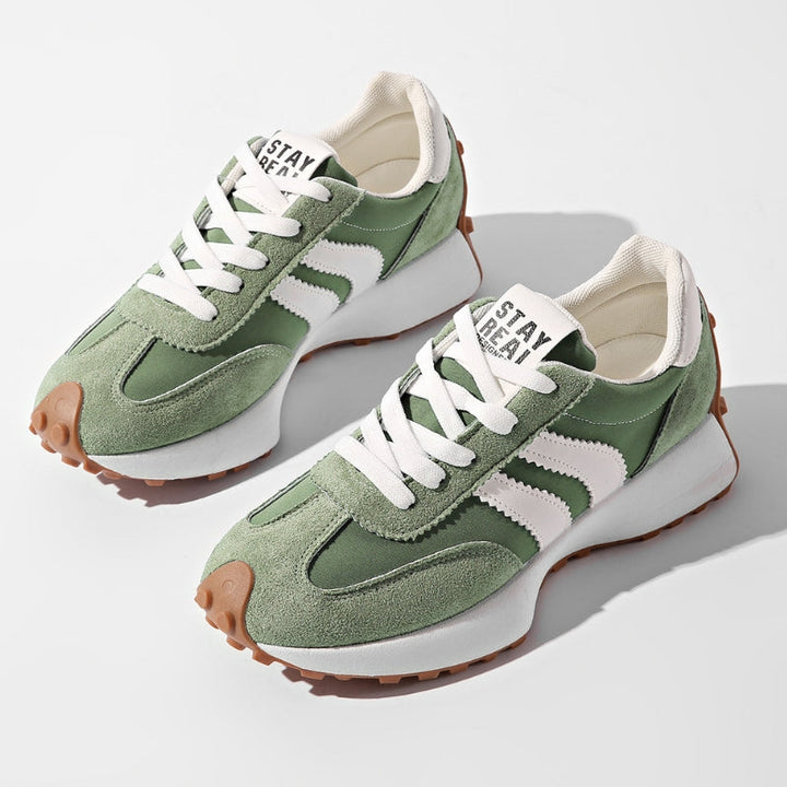 Et par grønne ruskindssneakers med hvide striber og hvide snørebånd set skråt ovenfra på hvid baggrund 1