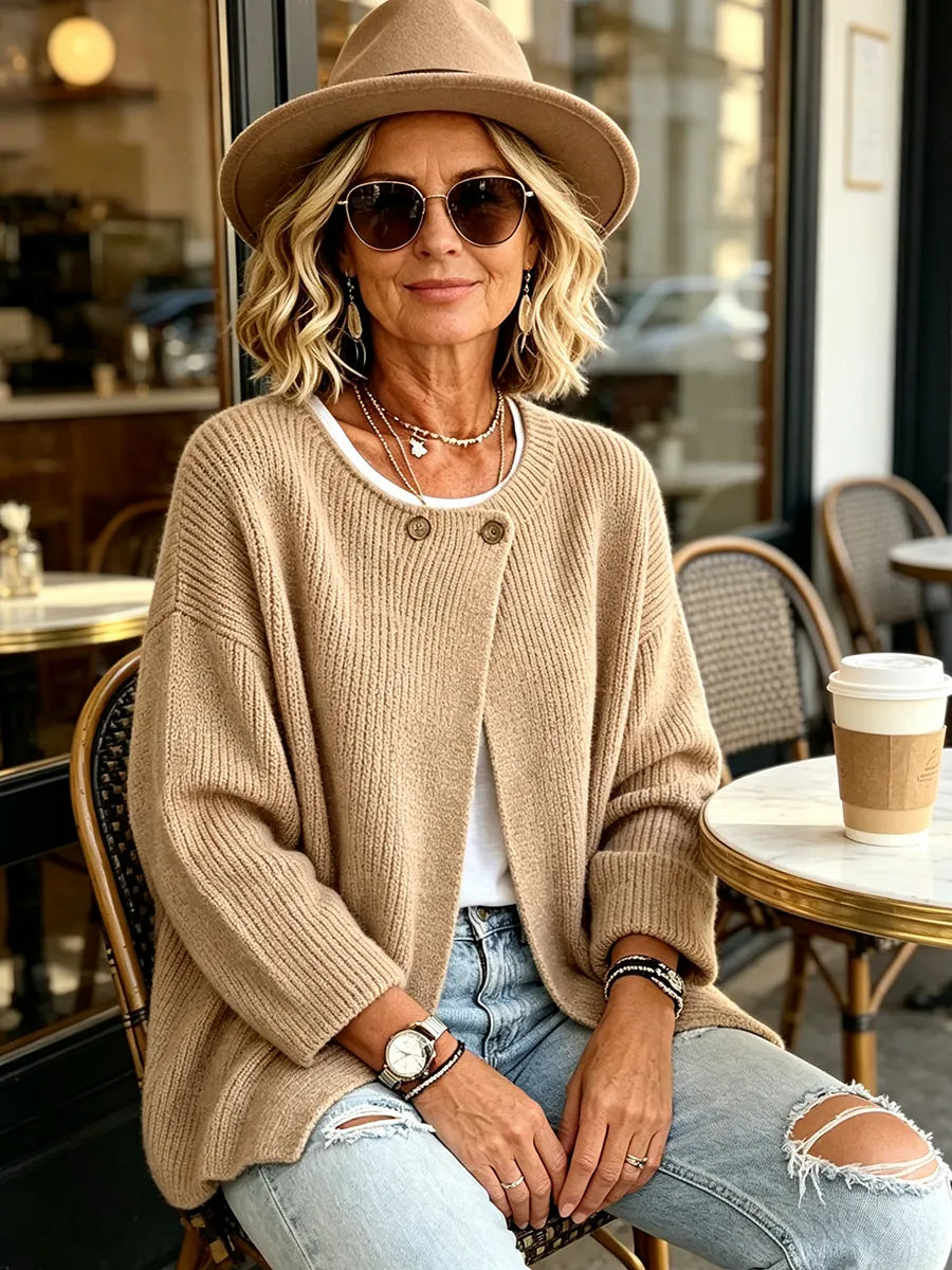 Model i kamelfarvet cardigan, hat og solbriller sidder ved et cafébord udendørs 5