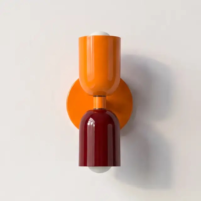 Væglampe med klar orange øverste skærm og vinrød nederste skærm på en orange rund vægplade, set forfra mod lys væg. 25