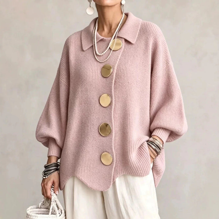 Model i rosa ribstrikket cardigan med store guldfarvede knapper og bølgekant, båret med hvide bukser. 6