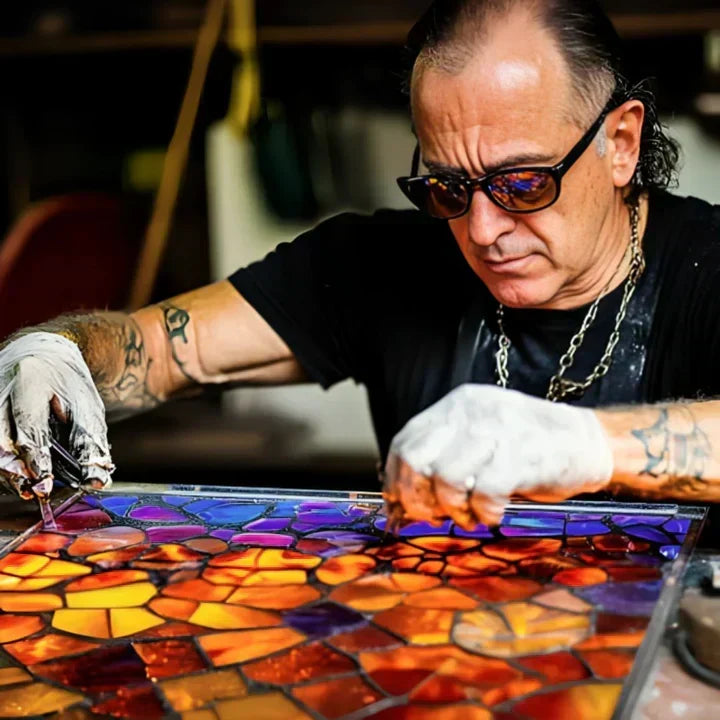 Tatoveret håndværker med solbriller lægger farvede glasstykker i et orange og lilla mosaikmønster 2