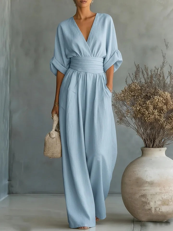 Jumpsuit i lyseblå set forfra på model med hånden i lommen, strikket taske og vase med tørrede blomster 2