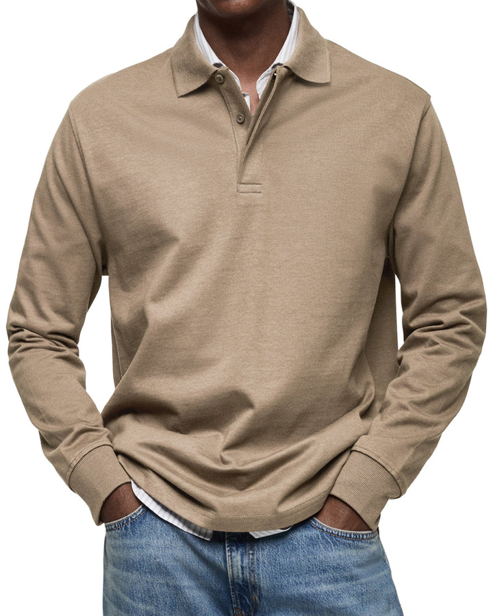Langærmet poloshirt i sandbeige, båret af en model med stribet skjorte under og jeans, set forfra. 8