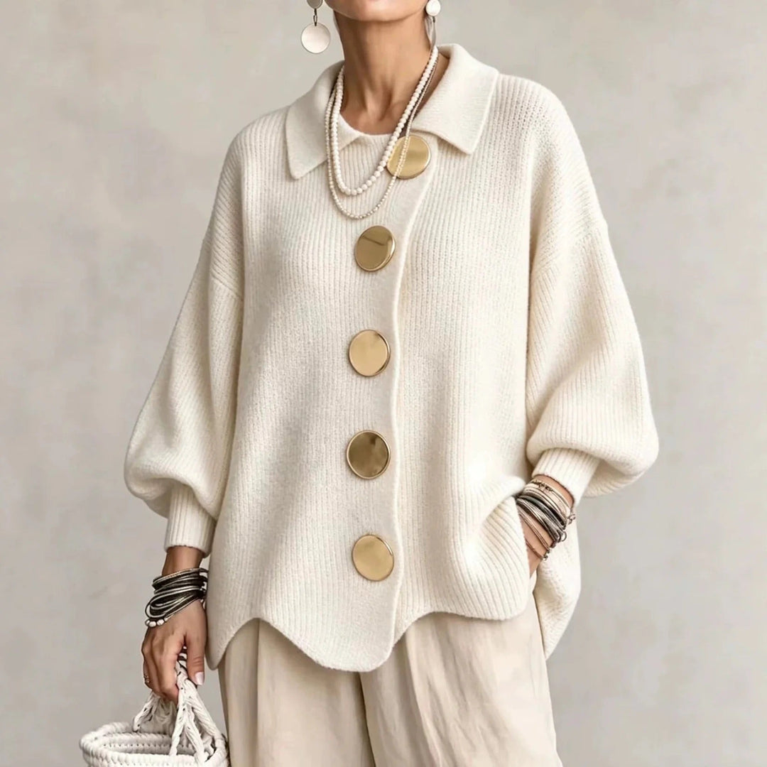 Model i cremehvid ribstrikket cardigan med store guldfarvede knapper og bølgekant, båret med beige bukser. 4