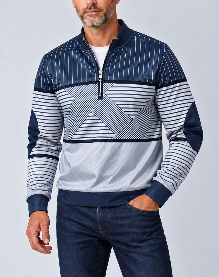 Mand med gråt skæg i marineblå og hvid stribet pullover med halv lynlås, hånden i lommen på mørke jeans. 1