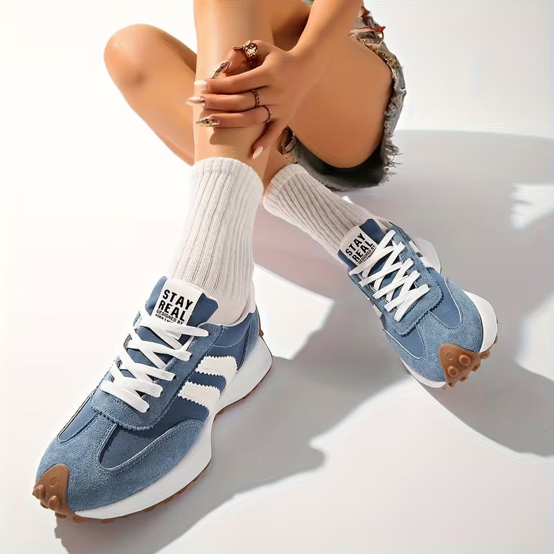 Model i hvide sokker og blå ruskindssneakers, siddende med krydsede ben på hvidt underlag 9