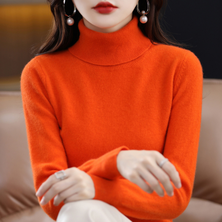 Model i orange rullekravesweater med hænderne foldet i skødet, set forfra fra hage til talje. 10