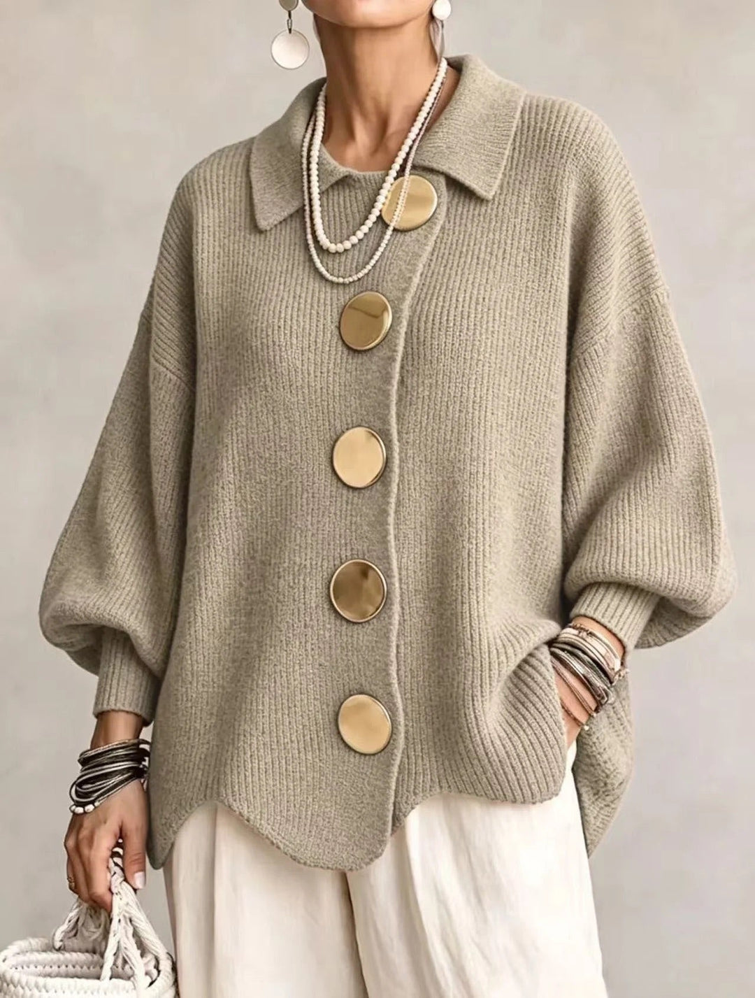 Model i grågrøn-beige ribstrikket cardigan med store guldfarvede knapper, spids krave og bølgekant, set forfra. 17