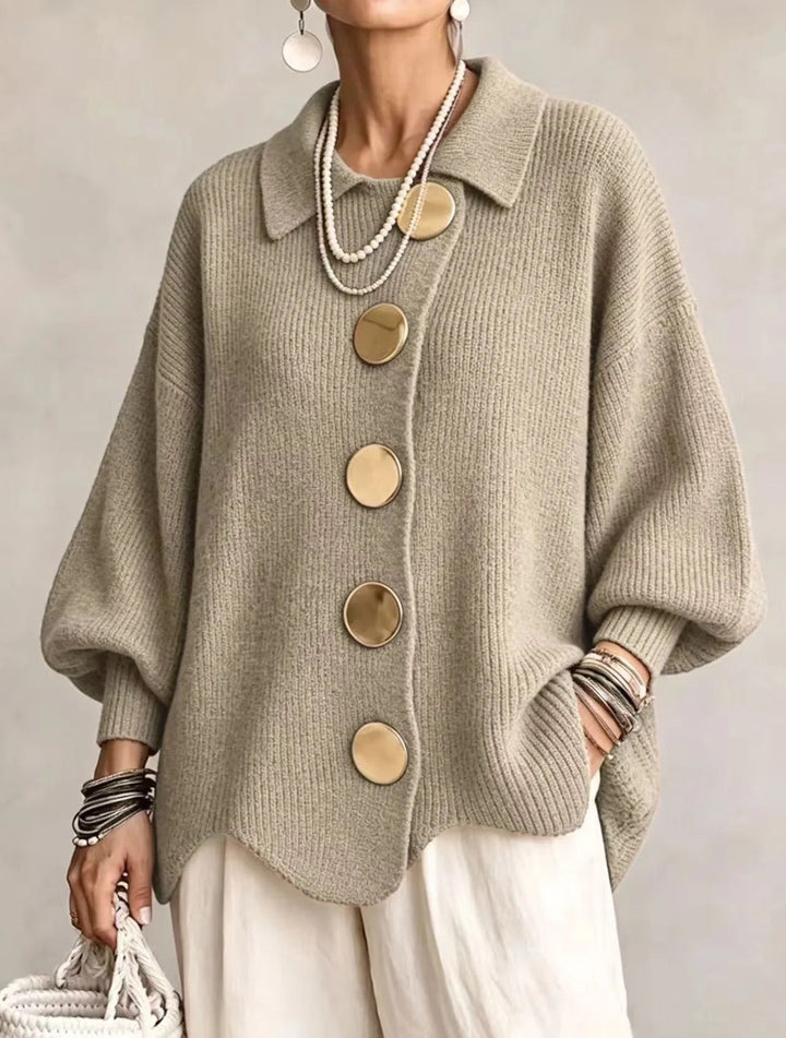 Model i grågrøn-beige ribstrikket cardigan med store guldfarvede knapper, spids krave og bølgekant, set forfra. 17