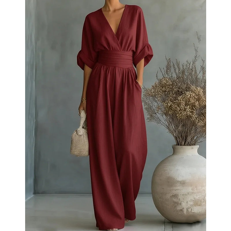 Mørkerød jumpsuit set forfra på model med hånden i lommen, vide ben og vase med tørrede blomster 8
