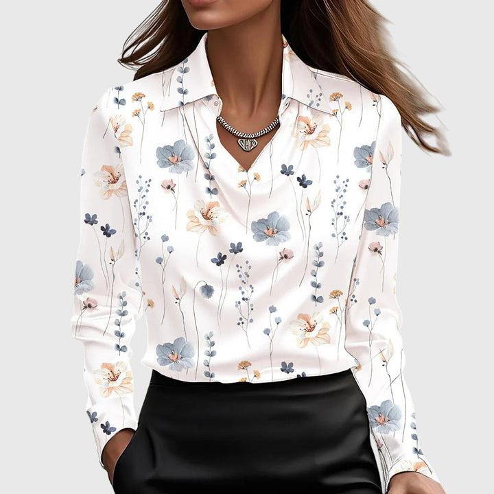 Model i hvid satinbluse med fint mønster af små blå, fersken og lyserøde blomster, vandfaldsudskæring og krave. 9