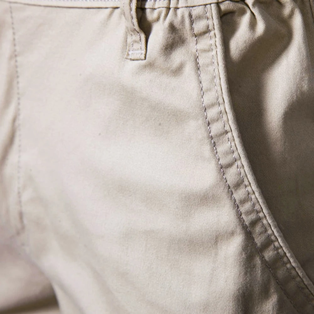 Nærbillede af sidelommen og bælteløkken på beige shorts med tydelige kontrastsyninger. 3