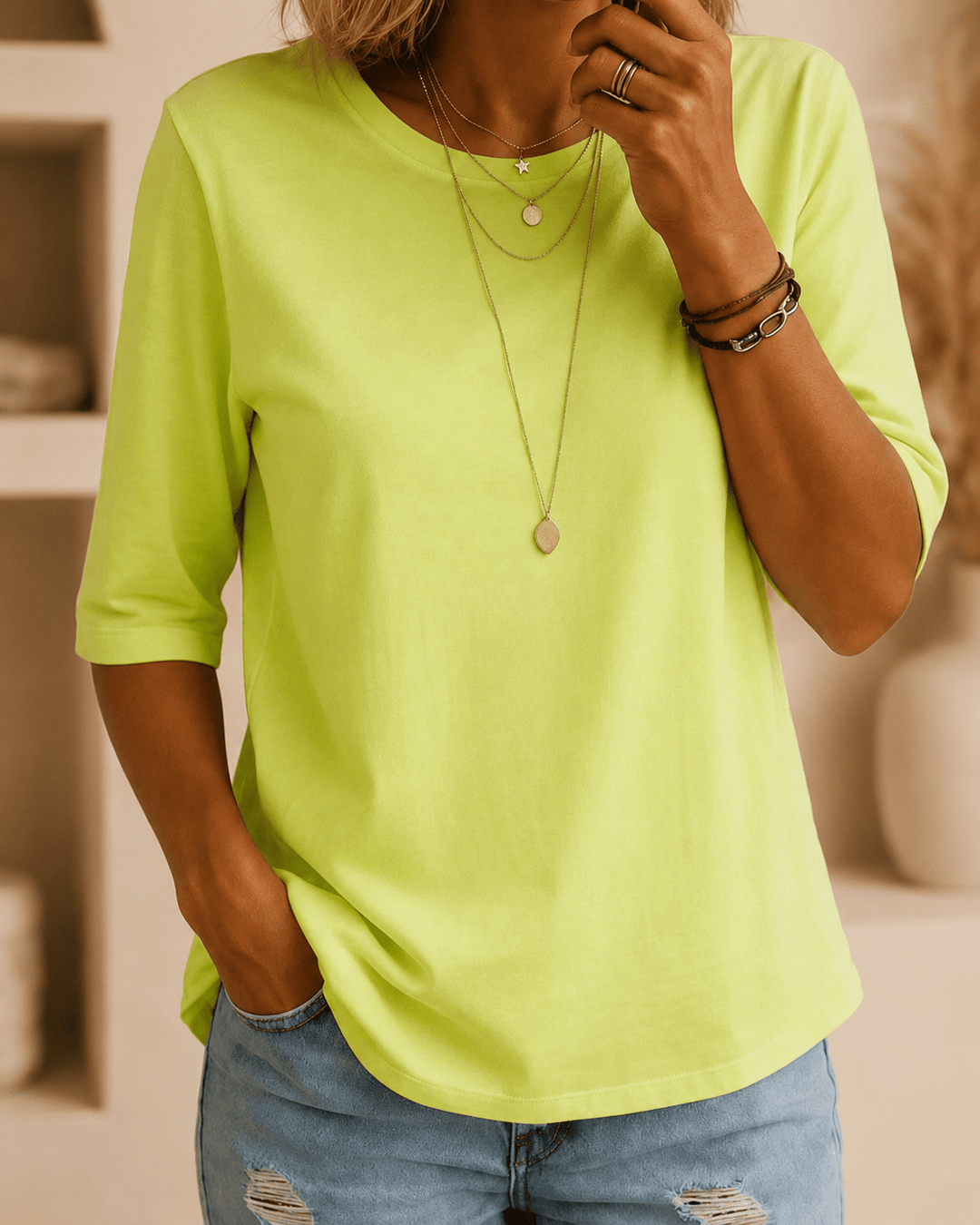 Model i neongrøn t-shirt med halvlange ærmer og rund hals, stylet med lyse jeans, lagdelte halskæder og armbånd. 1