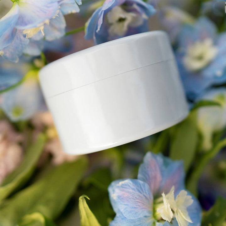Hvid rund indsats ligger ovenpå blå og hvide rittersporeblomster og grønne blade. 9