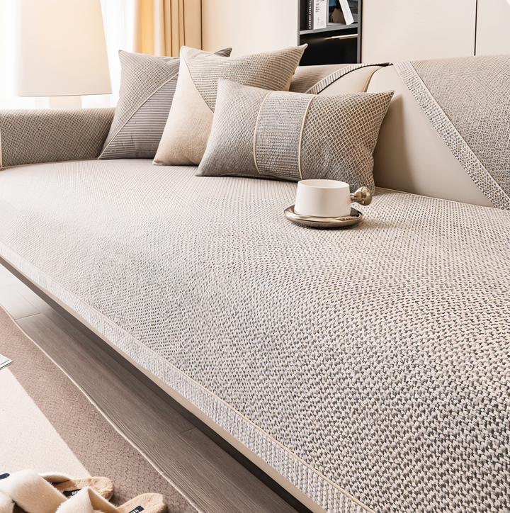 Betrækket i beige og grå vævet struktur på en sofa med puder og en hvid kop på sædet. 1