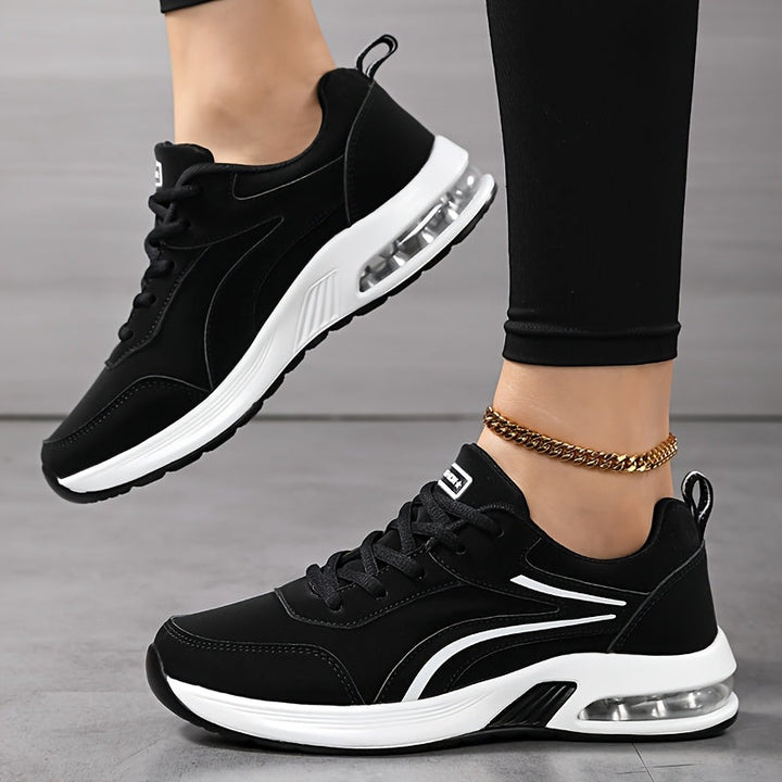 Sorte sneakers med hvide sidestriber og gennemsigtig luftpude i hælen, set fra siden på model med det ene ben løftet. 3