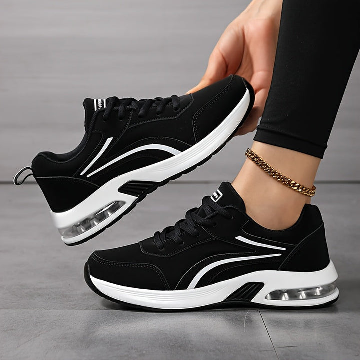 Sorte snørede sneakers med hvid sål og synlig luftpude, båret af model, der løfter det ene ben og viser siden af skoen. 1