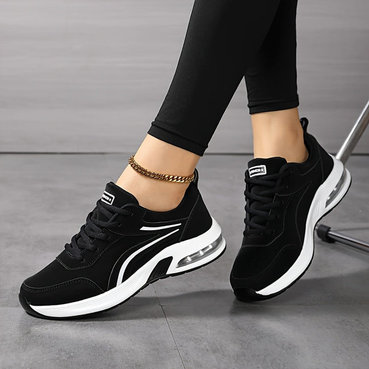 Model sidder med krydsede ben og viser et par sorte snørede sneakers med hvid luftpudesål set fra siden. 5