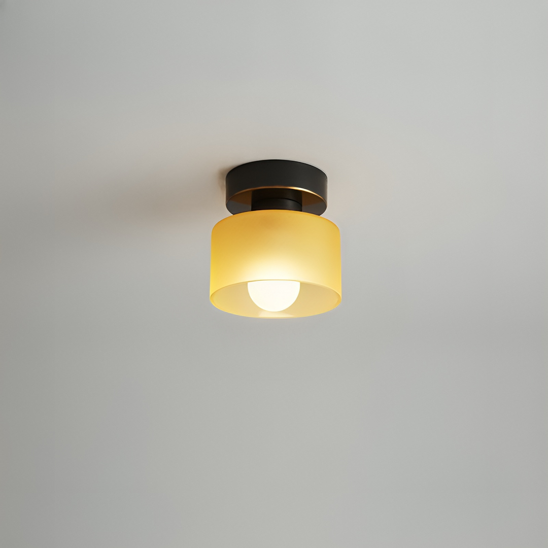 Loftspot med sort fatning og gul mat glasskærm, tændt og set tæt på mod gråt loft. 8