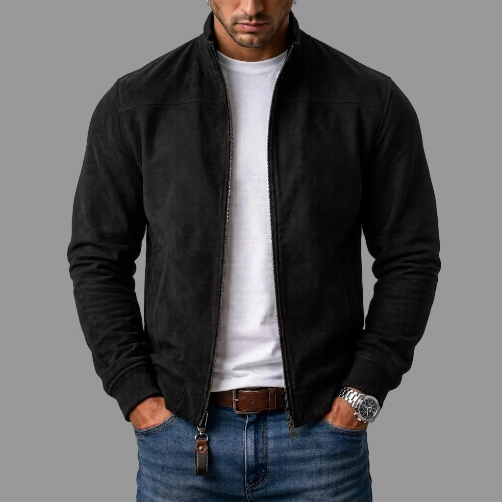 Model i sort jakke i ruskindslook, åben lynlås, hvid t-shirt, jeans og læderrem; lynlåsen har en brun læderlap. 1