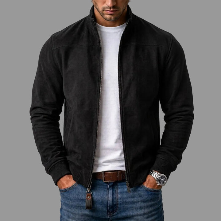 Model i sort jakke i ruskindslook, åben lynlås, hvid t-shirt, jeans og læderrem; lynlåsen har en brun læderlap. 1