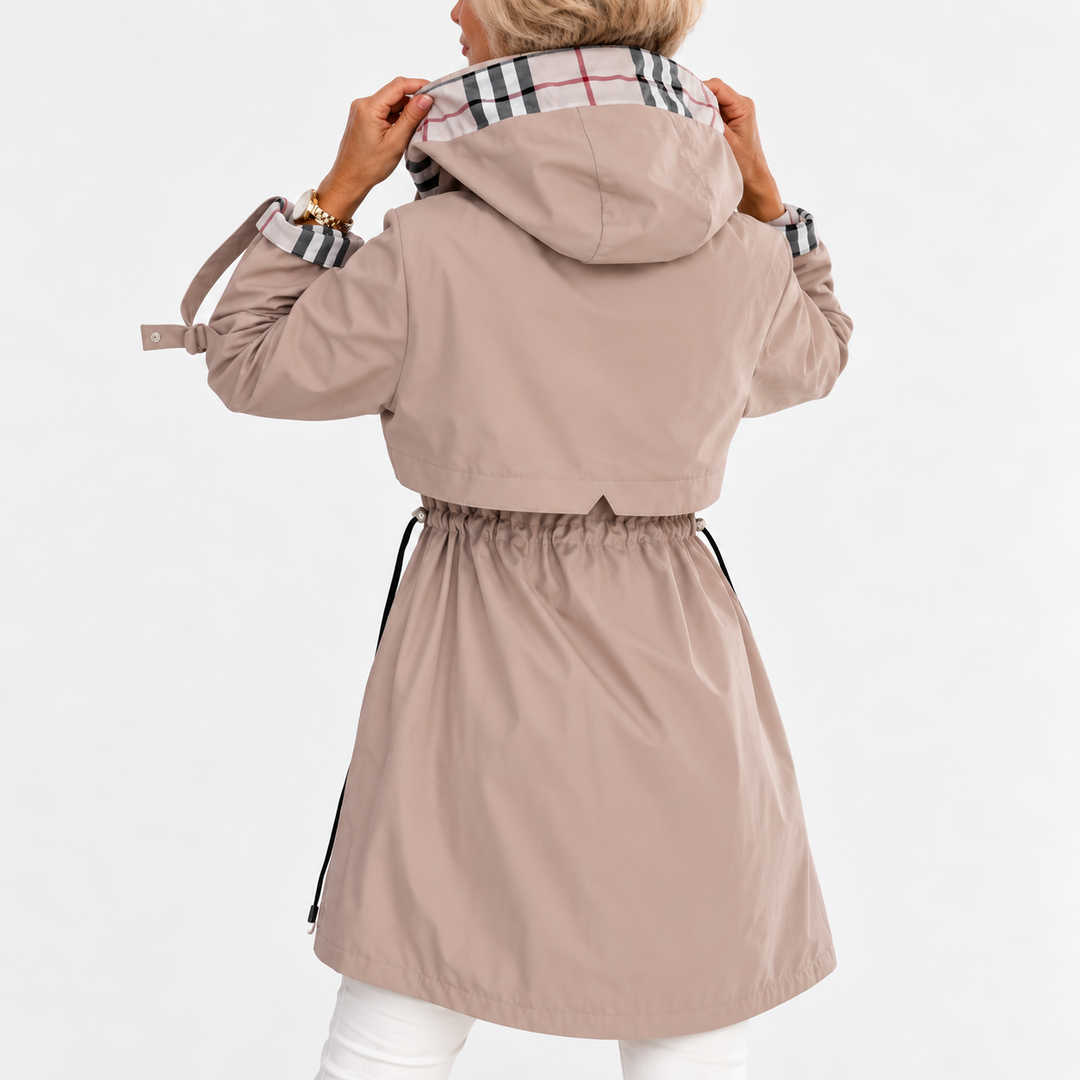 Frakken i beige set bagfra, model holder hætten med ternet foer, sammentrukket talje og korte ærmestropper. 3