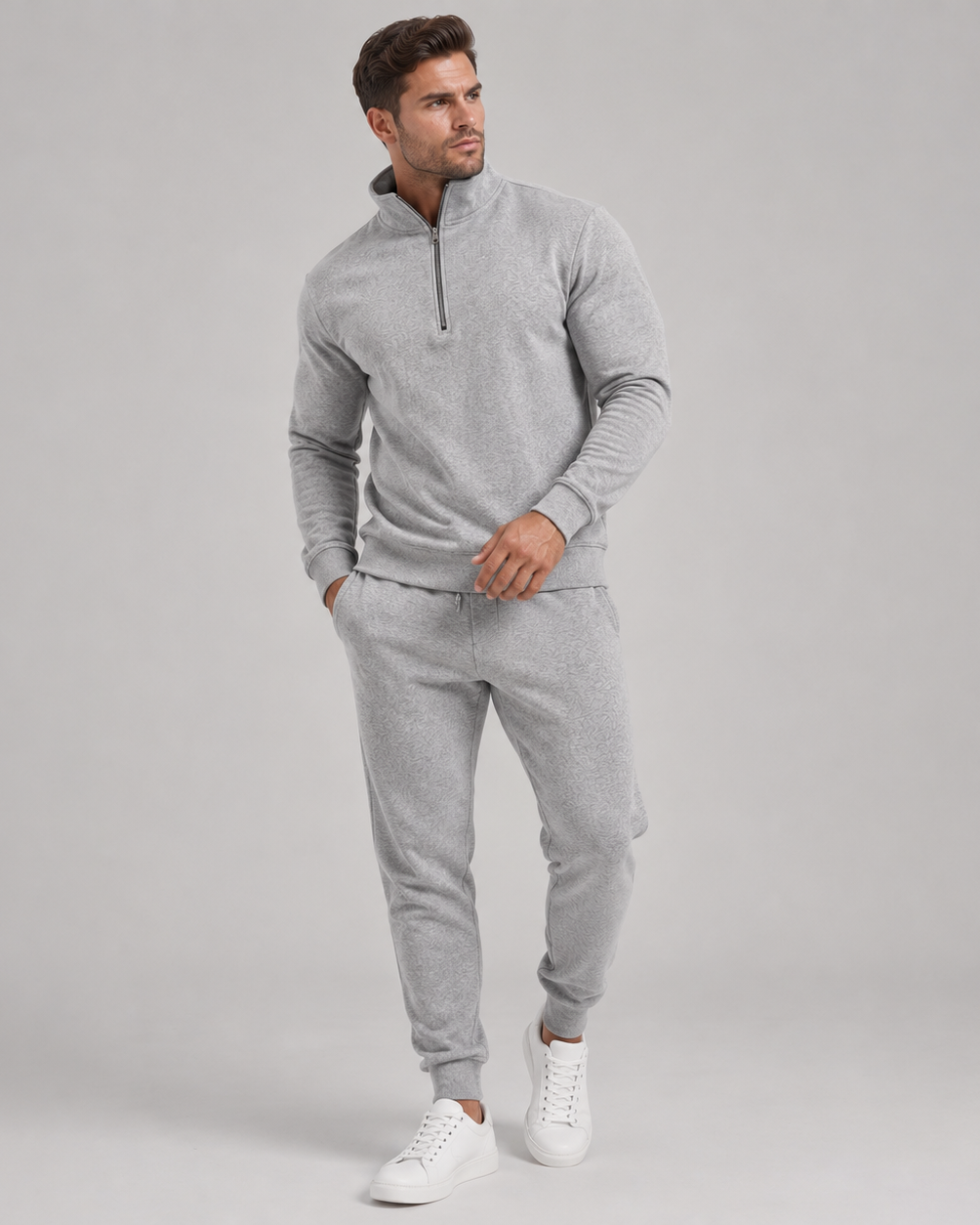 Mand i helfigur iført lysegråt sæt med halv lynlås og joggingbukser samt hvide sneakers 1