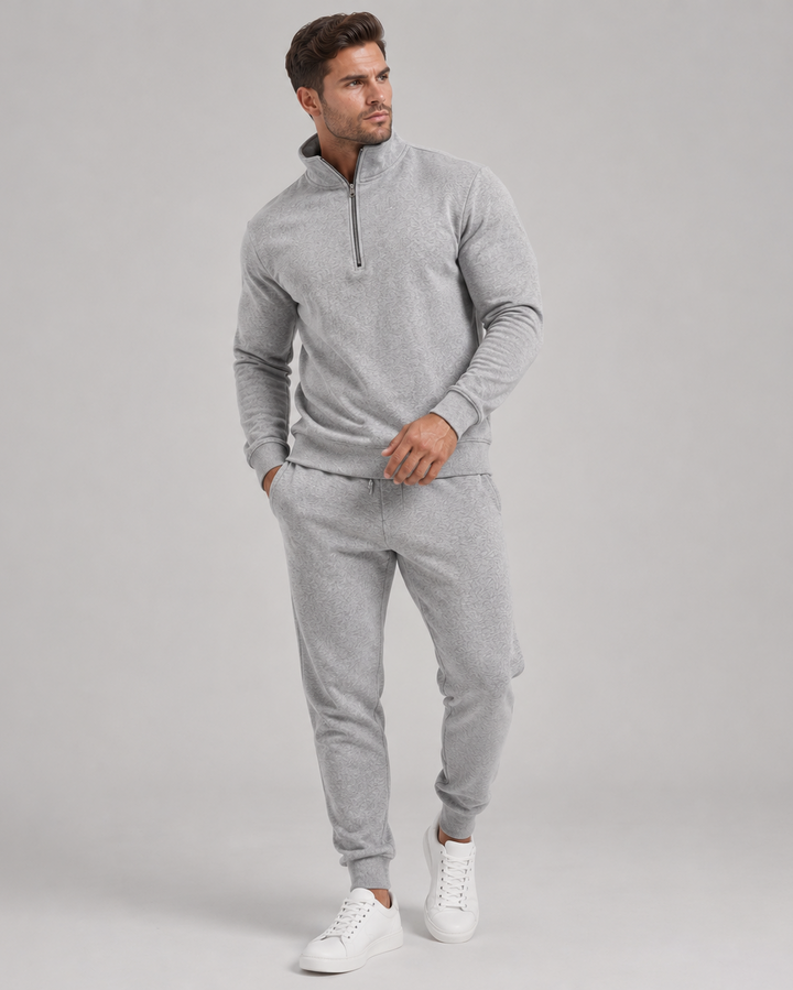 Mand i helfigur iført lysegråt sæt med halv lynlås og joggingbukser samt hvide sneakers 1