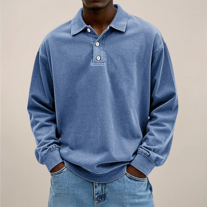 Model set forfra i blå langærmet polotrøje med knapper og ribkant, hænderne i lommerne på lyse jeans. 1
