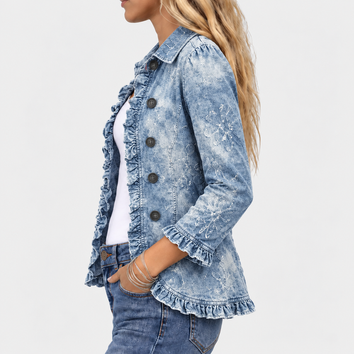 Sidebillede af den blå denimjakke med flæser ved ærmekant og bund samt blomsterprint på ærmet 3