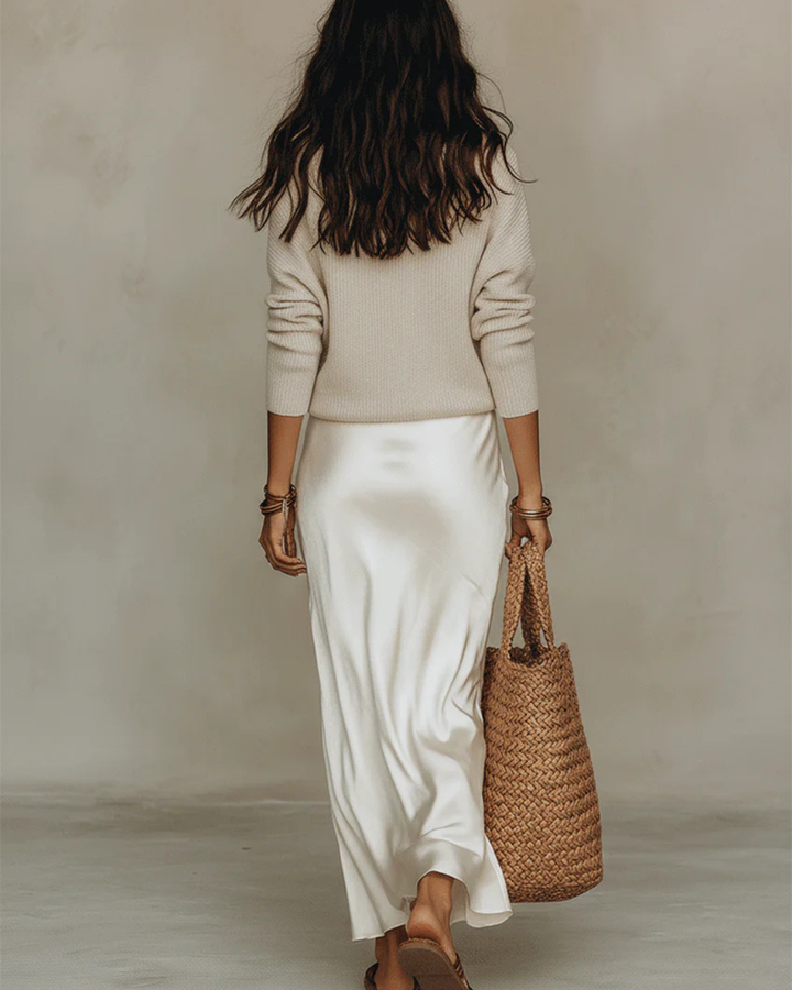 Model set bagfra i cremehvid satinkjole og beige striktrøje, med flettet taske og sandaler 9