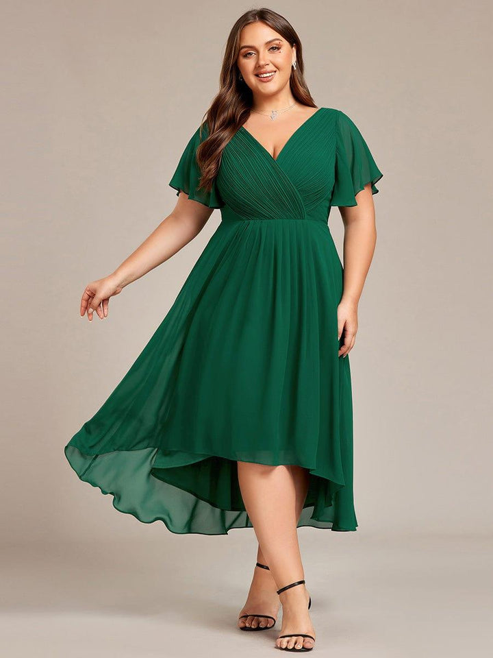 Mørkegrøn chiffonkjole i plussize på model, set forfra med svingende asymmetrisk nederdel og sorte sandaler. 36