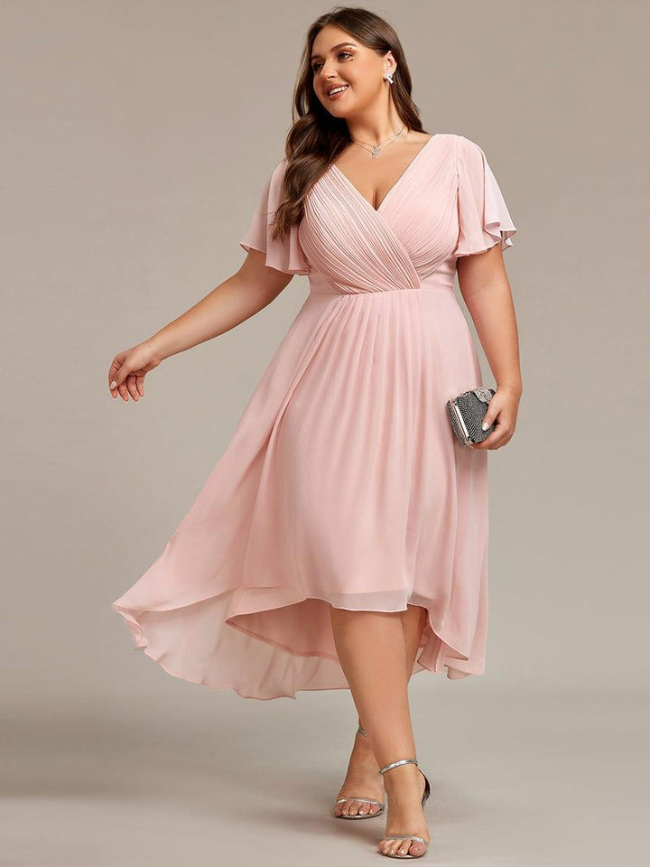Lyserød chiffonkjole i plussize på model med glitrende clutch og sølvfarvede sandaler, set forfra i bevægelse. 31