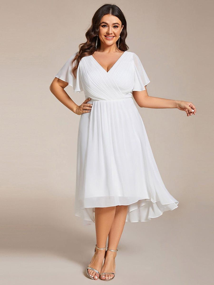 Plus size-model i hvid kjole med hånden på hoften, V-hals, flagrende ærmer og asymmetrisk fald. 73