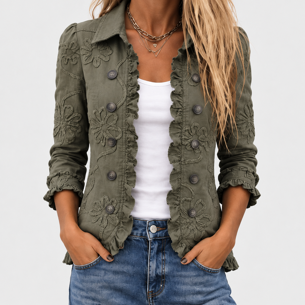 Nærbillede af den olivengrønne jakke på en model med hvid top og jeans, med blomsterbroderi, knapper og flæsekant langs fronten. 1
