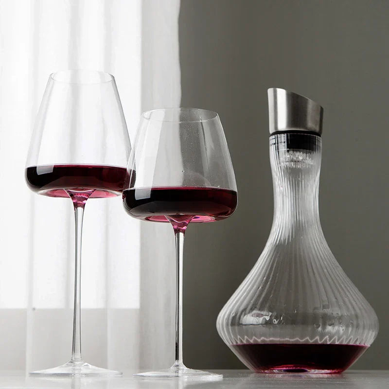 To glas med rødvin ved siden af en riflet karaffel foran et lyst gardin 3