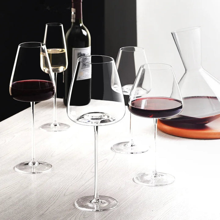 Rødvinsglas, champagneglas og karaffel på et lyst træbord, set fra siden med flasken bagved 6