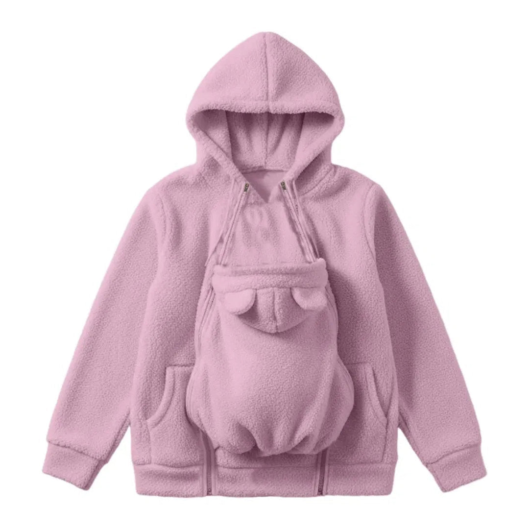 Lyserød hættetrøje i sherpa-fleece set forfra som flat lay, med babybærepanelet med bjørneører lynet fast på maven. 1