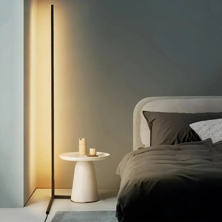 Tændt sort gulvlampe med varmt lys ved siden af en seng og et rundt hvidt sidebord 1