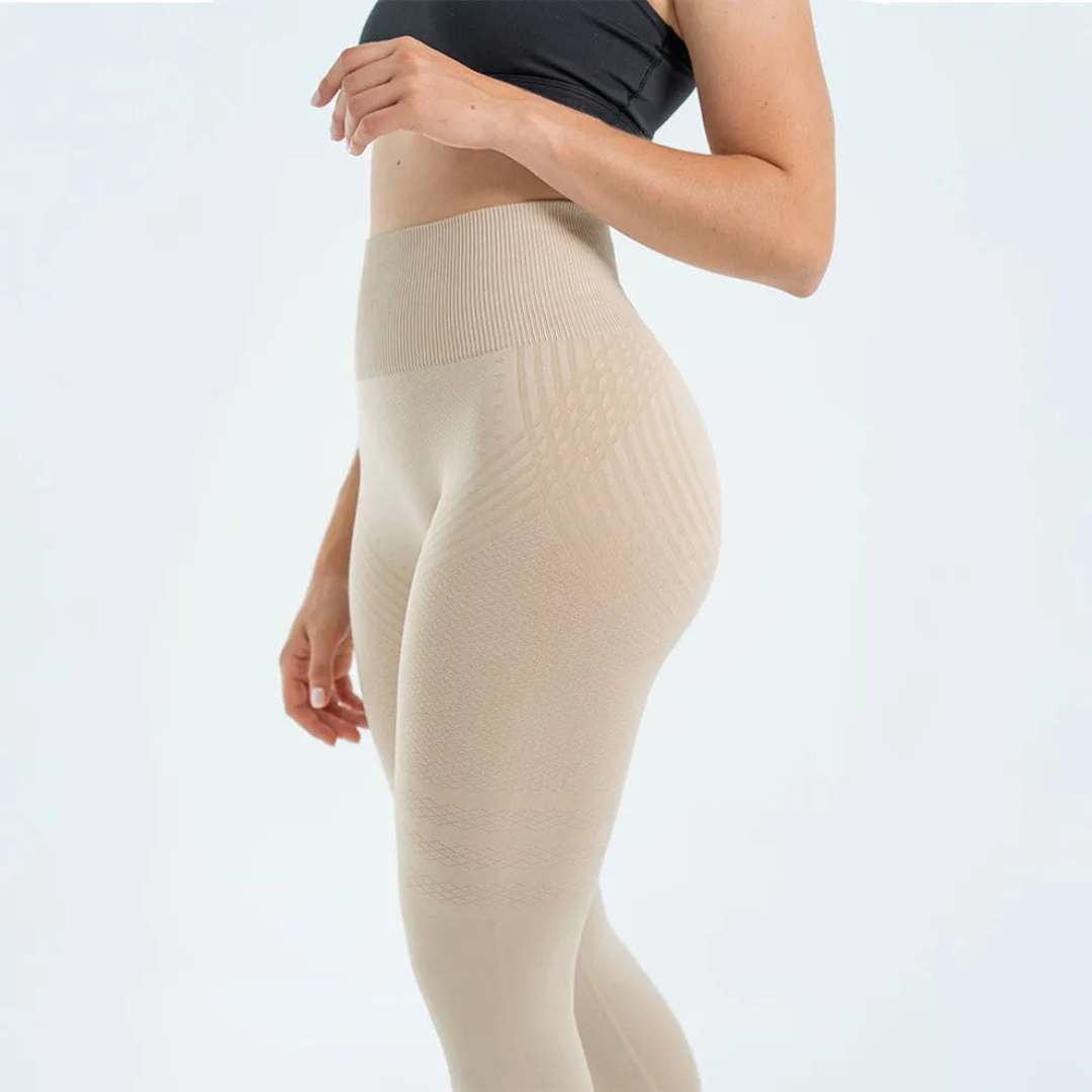 Sidebillede af model i beige sømløse leggings med bred ribbet linning og mønstret strikstruktur over hofte og lår. 2