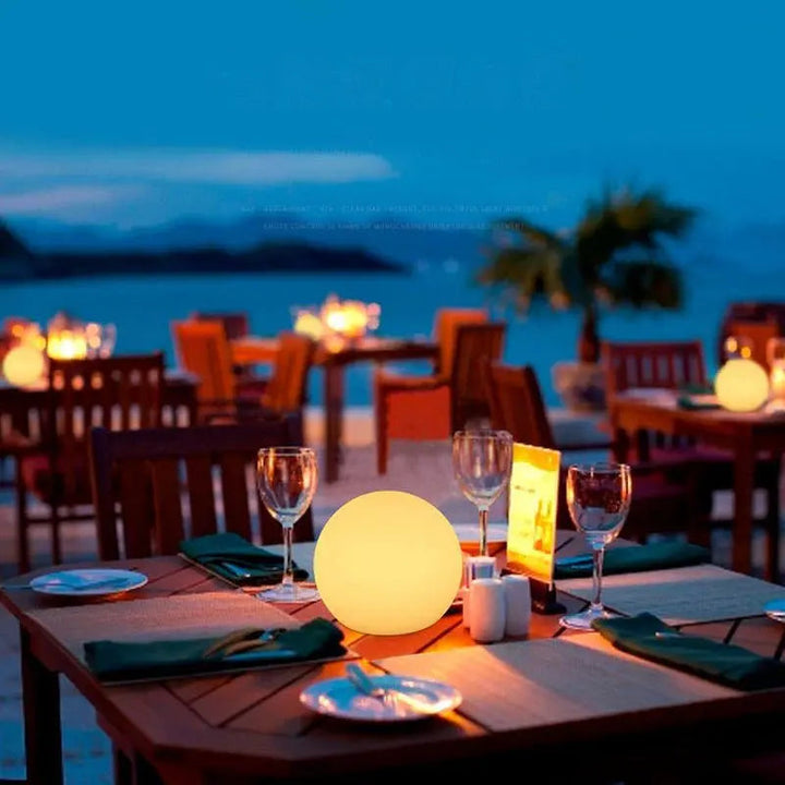 Gulligt lysende kuglelampe på et dækket bord på en restaurantterrasse ved havet i aftenskumringen. 5