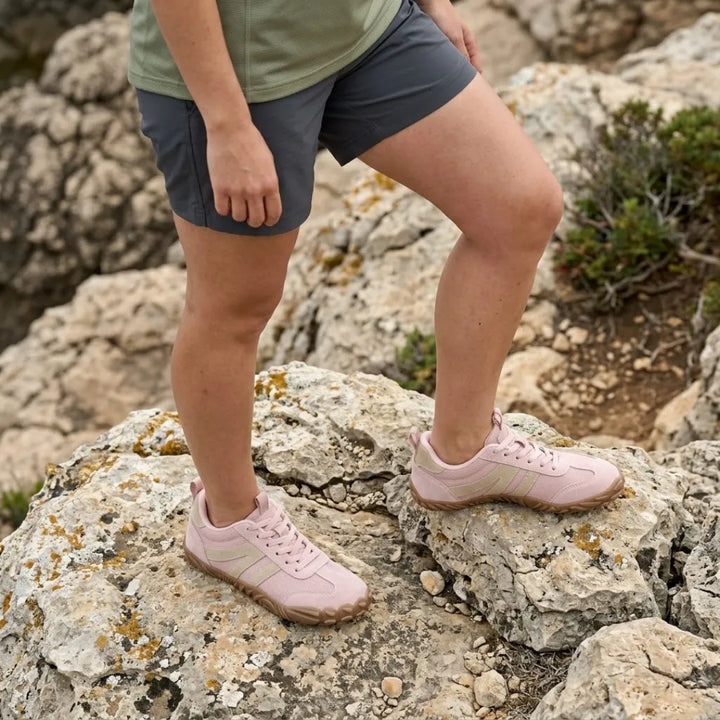 Model i grå shorts står på kalkklipper iført rosa sko med beige striber og brun gummisål. 11